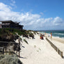 Photo of Surf Club building and beach view. Surf-lifesaving flags are set up on the beach with Surf-Lifesavers in the distance. Mobi-Fence is in the foreground running horizontally with the coastline and the ocean to help stop sand movement.