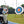 Photograph of a disabled archer on a blue Mobi- Path / Roadway that has been rolled out on grass, shooting an arrow at a bright target 