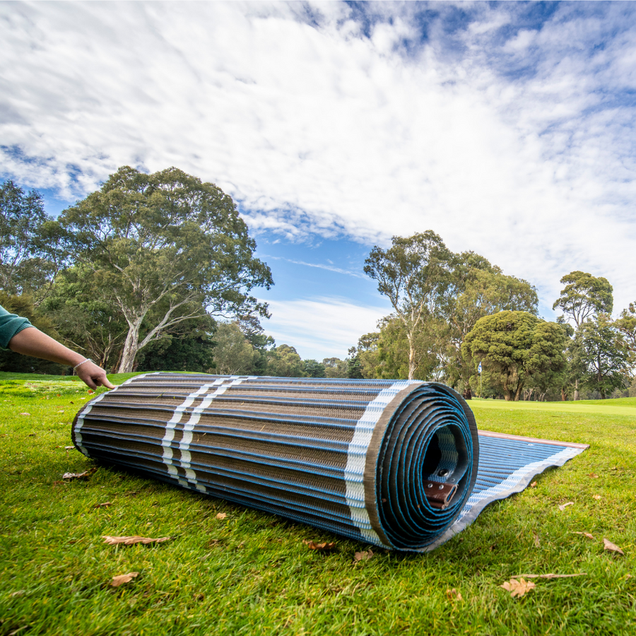 Photograpth of blue rolled up Mobi-road on grass. There is someone's arm in the shot using a finger to hold the mobi-road in place.
