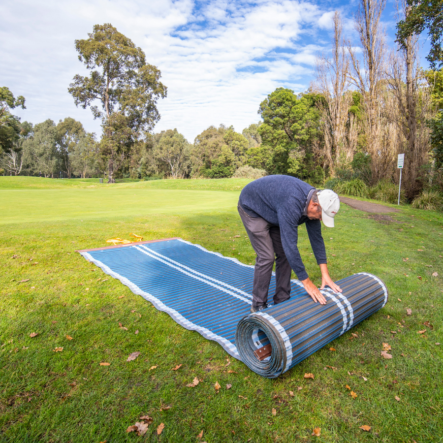 Photograph of Man rolling out blue Mobi-road on grass.