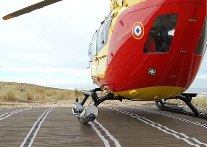 Back view of red and yellow helicopter that has landed on a Mobi-Heli Portable helipad that is set up on a beach