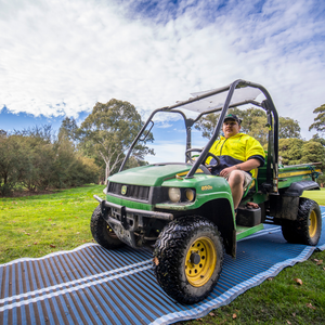 Photograph of man driving maintenance vehicle on a blue rolled out mobi-road placed on grass.
