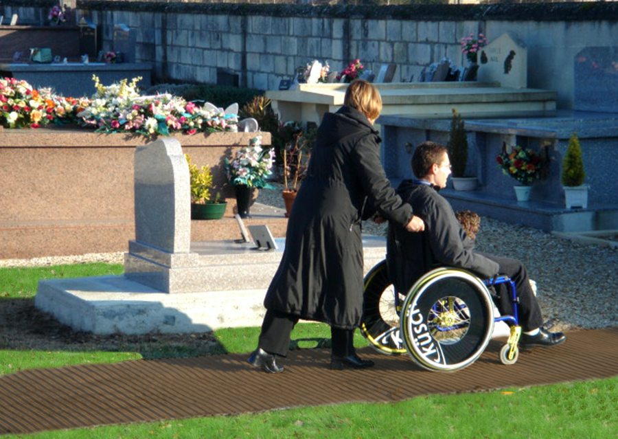 A disabled person in a wheelchair with a  dog on his lap is being pushed a long a brown Mobi- Path / Roadway that has been rolled out on grass in a cemetery