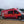 A red boat is being reversed into the sea by a red van which has reversed down a Mobi-Boat Ramp that was rolled out along the sand and into the water