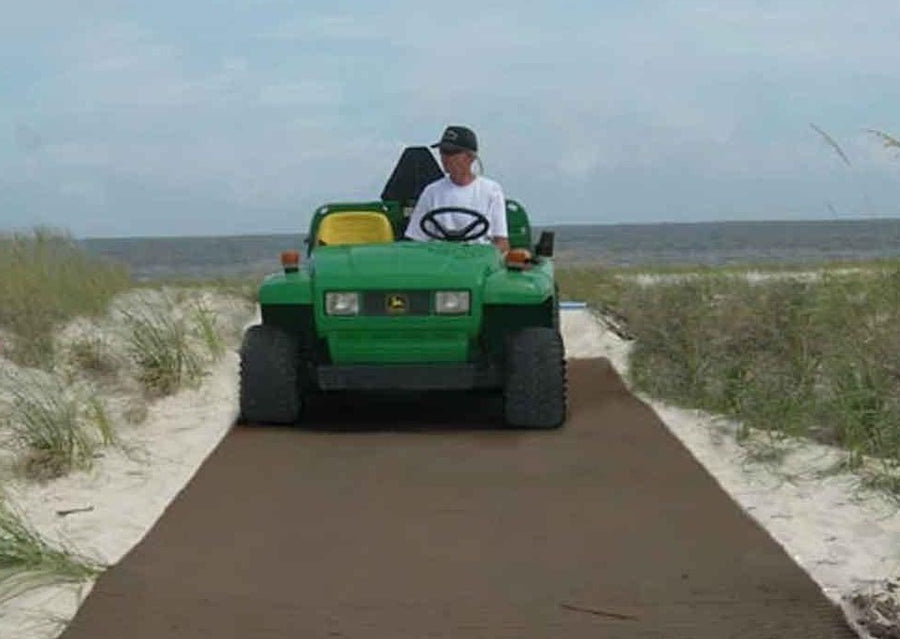 Brown Mobi-Boat Ramp has been rolled out on sand on a beach track. A boat attached to the back of a green beach buggy is being reversed  into the ocean   