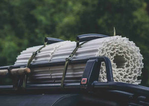 Photograph of a white Mobi-Track mat rolled up and tied to the roof racks of a car 