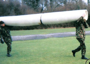Two people in military uniforms carrying a Mobi-Heli Portable helipad on their shoulders and walking across grass.