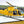 Yellow helicopter on a Mobi-Heli Portable helipad that has been rolled out on ground that is a combination of dirt and thin grass.