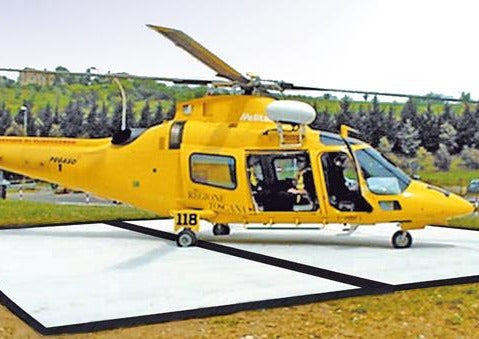 Yellow helicopter on a Mobi-Heli Portable helipad that has been rolled out on ground that is a combination of dirt and thin grass.
