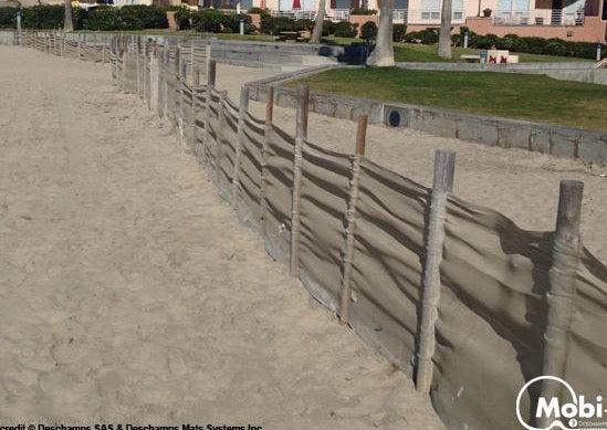 Photograph of a Mobi-Fence running along a beach with grass and houses in the background