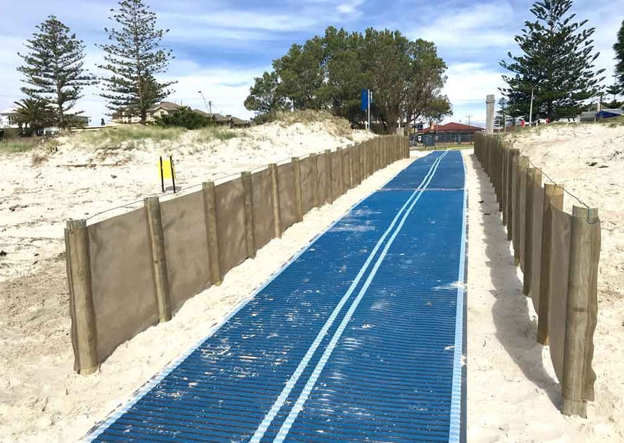 Photograph of access to a beach with Mobi-Fence running along each side of a blue Mobi-Path with two white lines down the middle to assist visually impaired people.